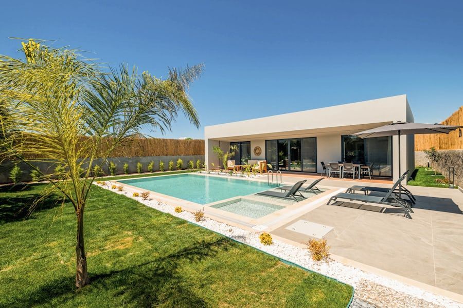 Modern backyard with a swimming pool, patio loungers, and a white house under a clear blue sky