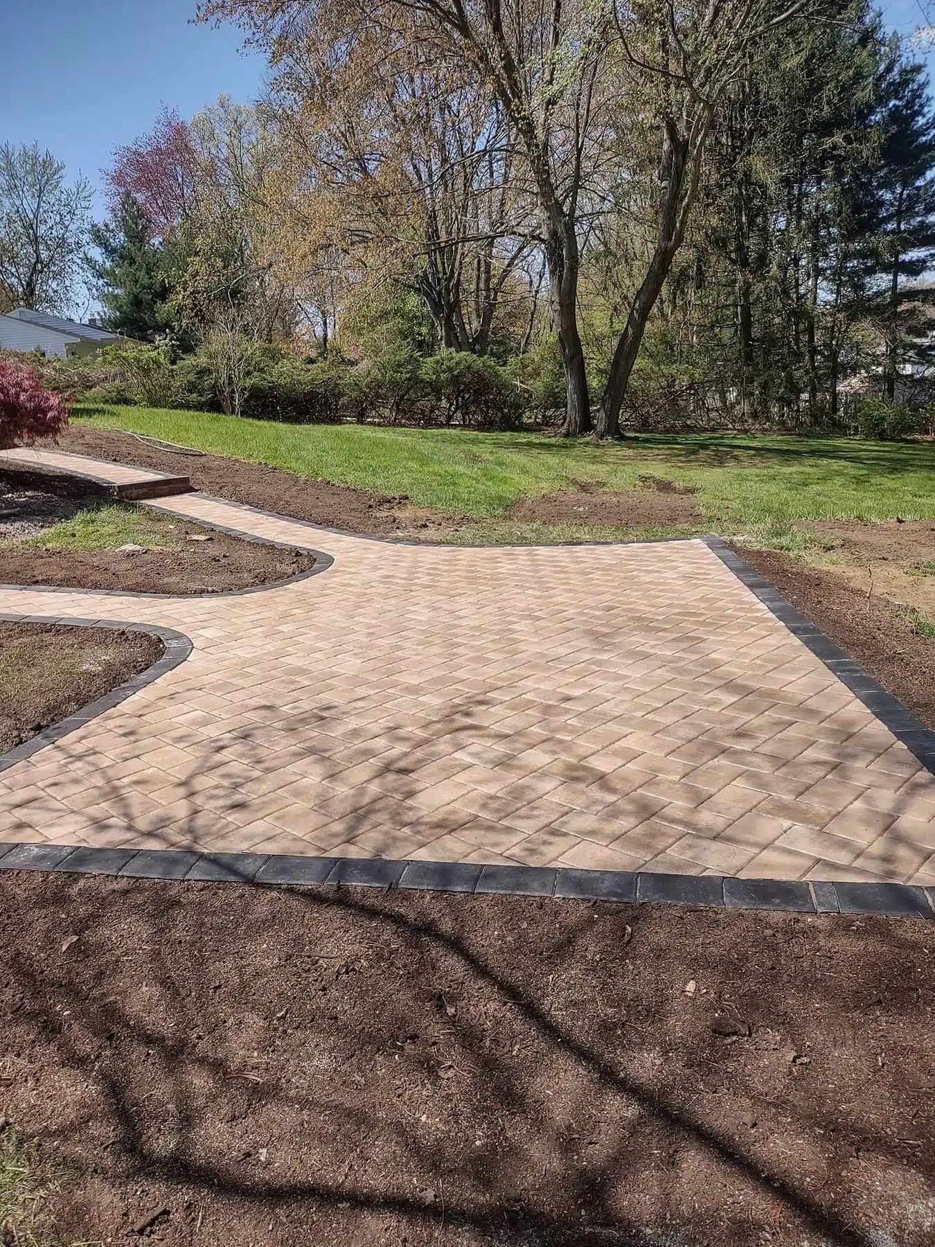 Stone-paved garden path beside a grassy slope with trees and shrubs on a sunny day