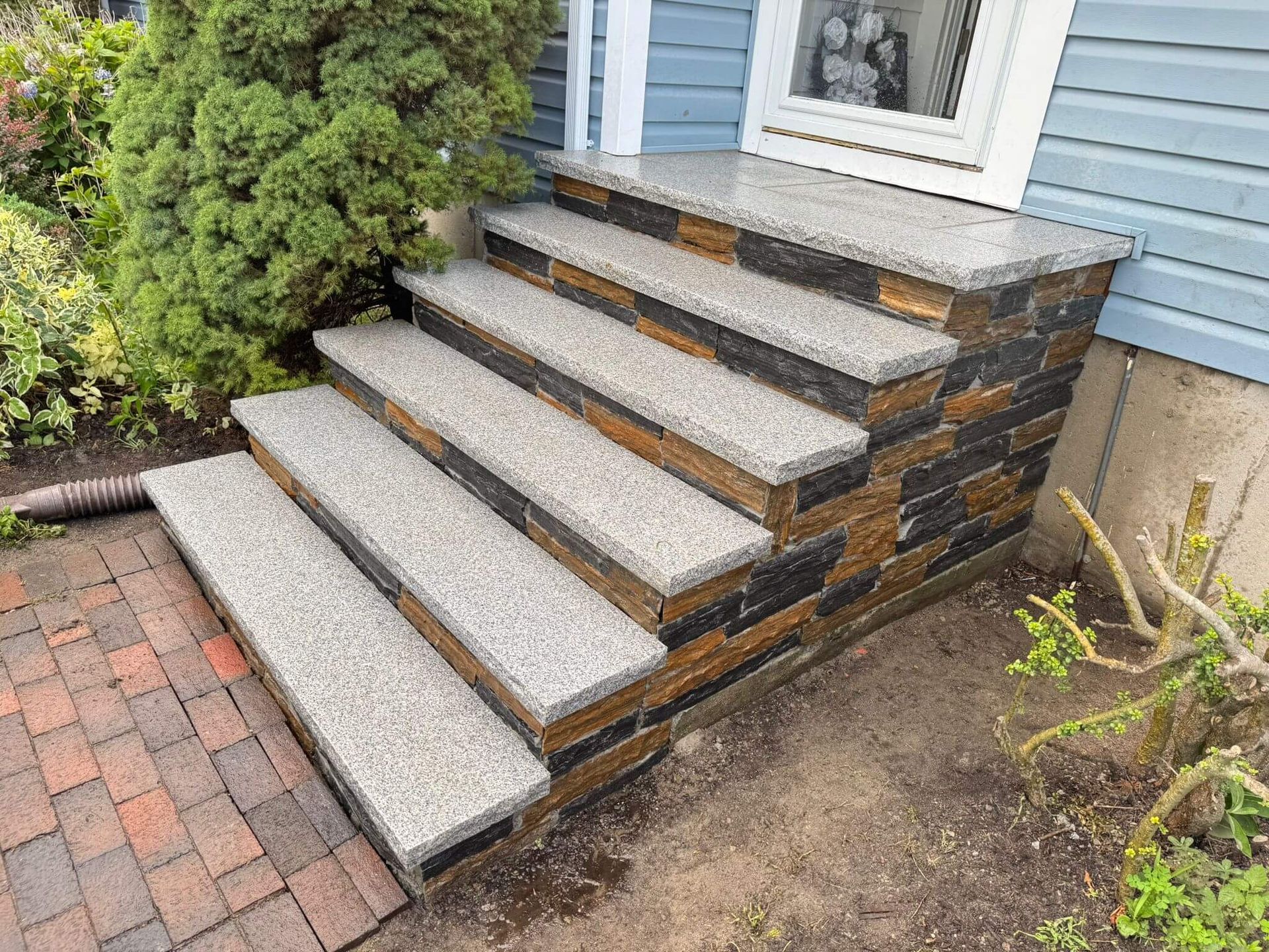 Front steps with gray concrete treads and brick sides leading to a blue house entrance.