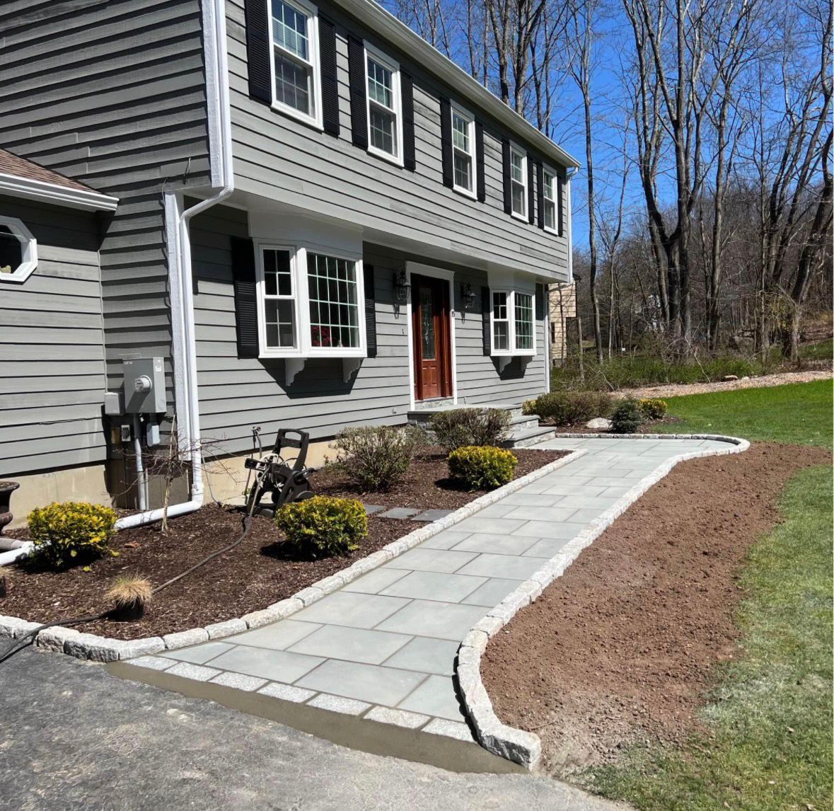 Gray house with white-trimmed windows and a stone walkway bordered by landscaping