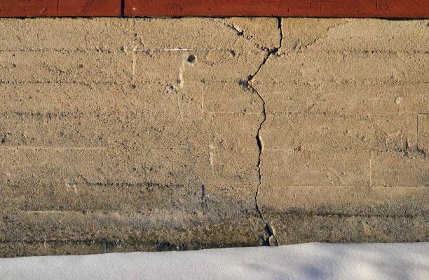 Close-up of a cracked beige stucco wall with a red brick edge above and concrete below.