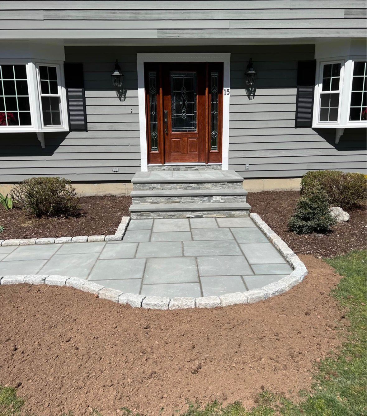 Front entry walkway with stone pavers and steps leading to a wood front door on a gray house