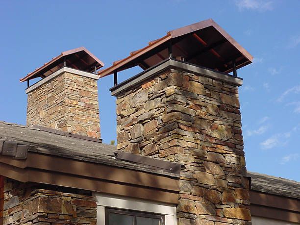 Stone chimneys with metal caps on a rooftop against a blue sky