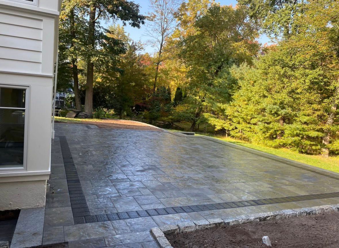 Freshly paved driveway beside a house, bordered by autumn trees and greenery
