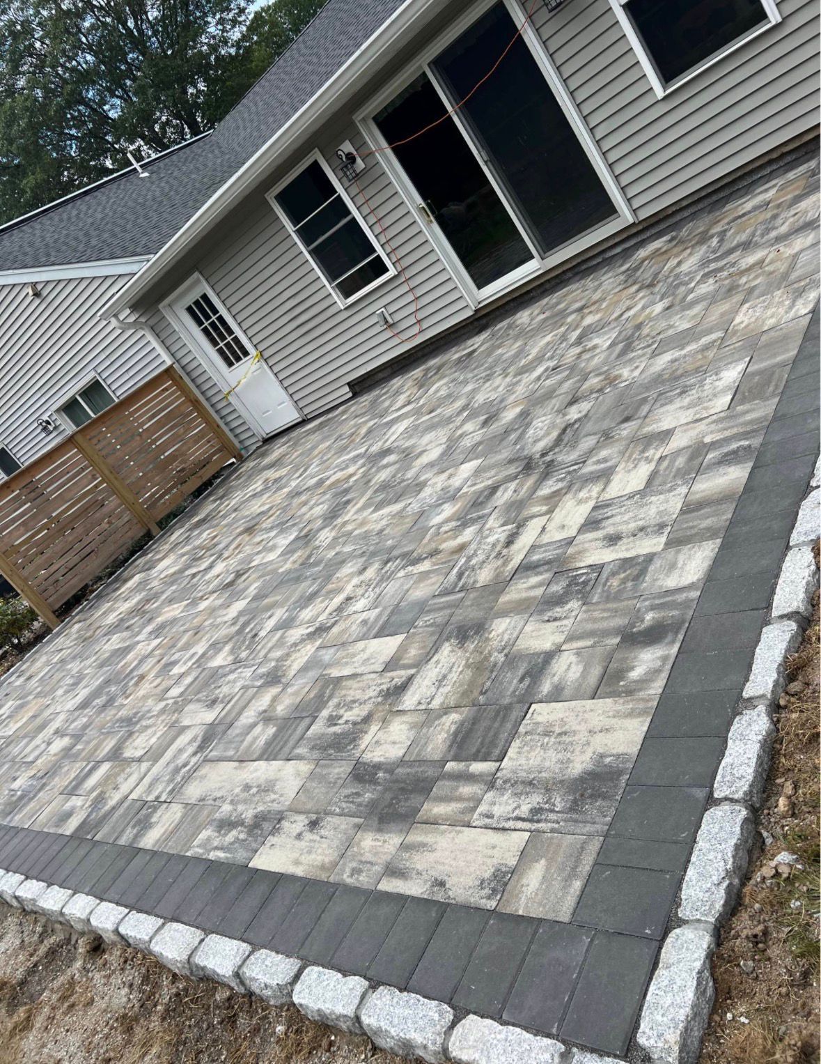Patio of gray patterned pavers beside a house with a screened porch and wooden fence