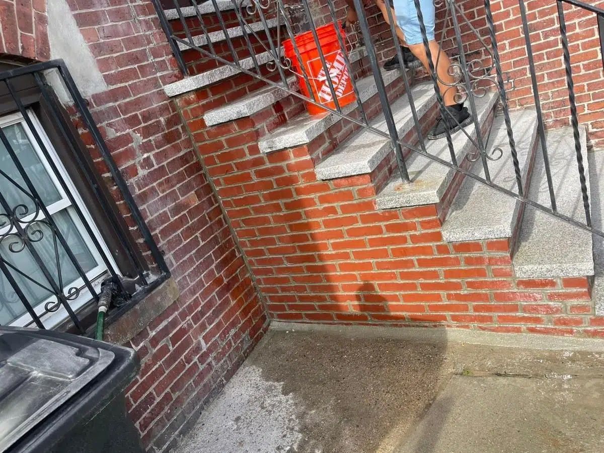 Brick stairwell and wet concrete landing beside a metal railing and basement door.