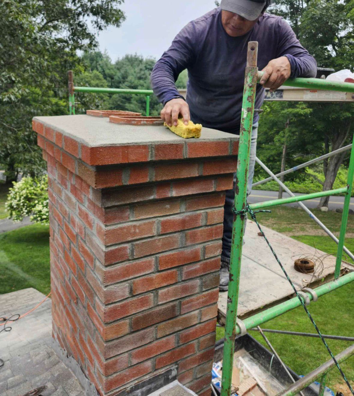 Person laying bricks on a chimney stack beside green scaffolding outdoors