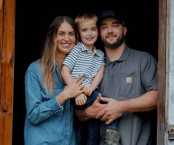 A family of three stands smiling in a doorway; the parents embrace a child between them against a dark background.