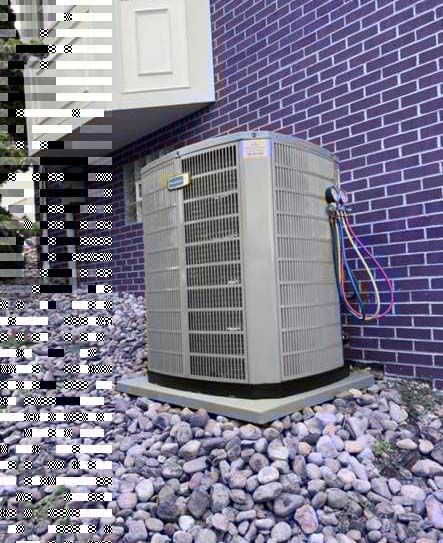 Outdoor air conditioning unit with technician gauge manifold attached, resting on gravel next to a purple brick wall.