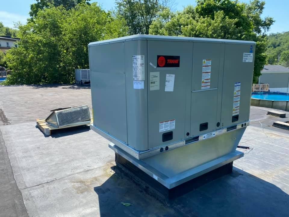 A Trane HVAC rooftop unit sits on a flat, gray commercial roof under a clear blue sky.