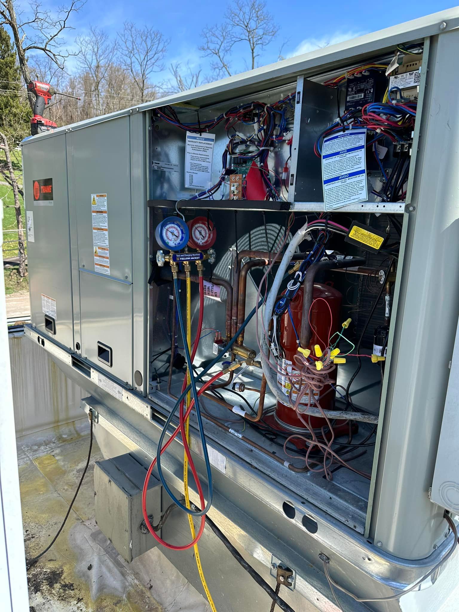 An outdoor HVAC unit with its side panel open, showing internal copper piping and a manifold gauge set connected for service.