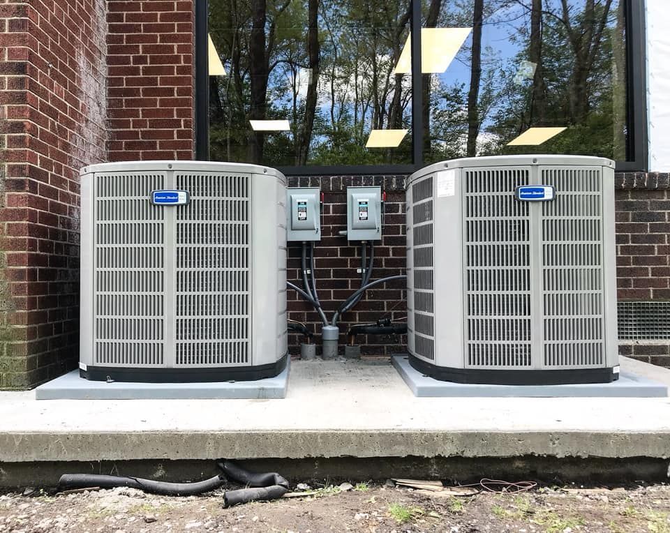 Two grey HVAC units sitting on concrete pads outside a brick building.