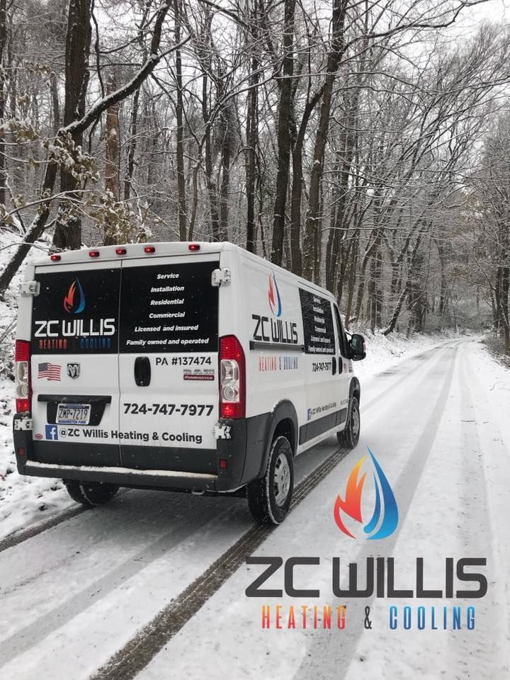 A ZC Willis Heating & Cooling white van parked on a snow-covered road lined with trees.