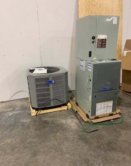 A new air conditioning condenser and a furnace standing on wooden pallets in a warehouse.