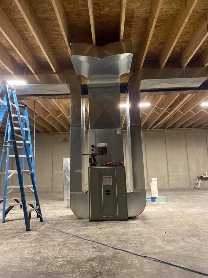 A metal HVAC furnace unit installed in an unfinished basement with ductwork branching to the ceiling joists.