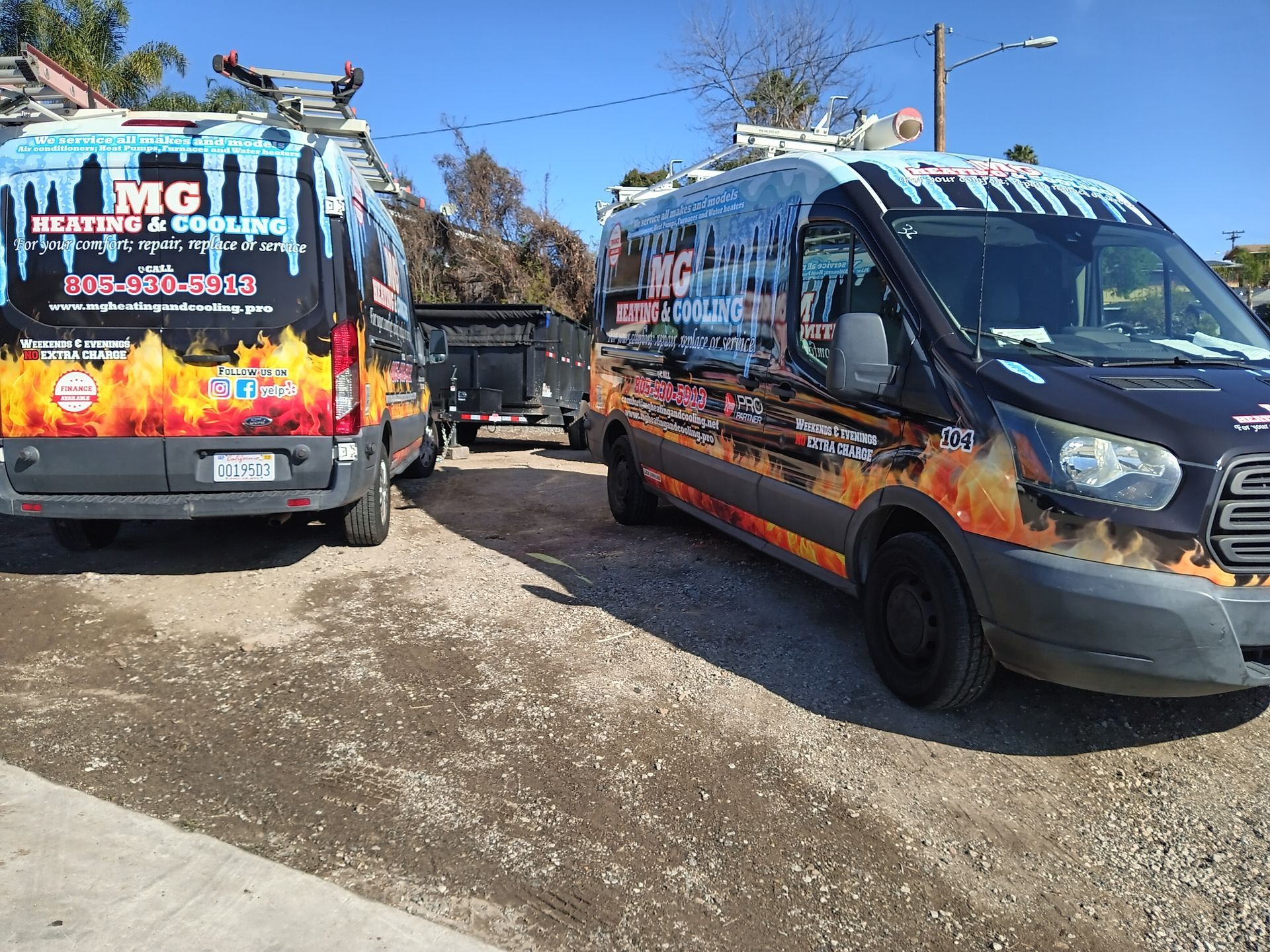 Two MG Heating & Cooling vans parked, with a trailer in between. Snowy/fiery graphics on dark vans.