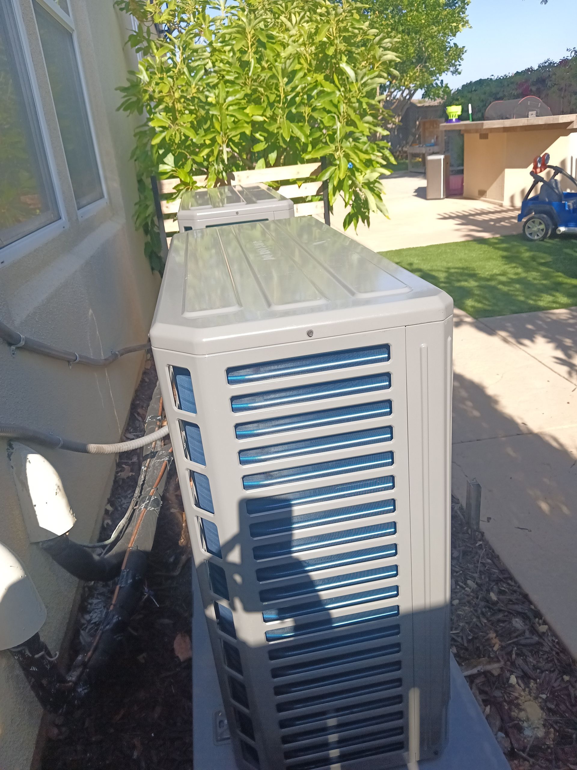 Air conditioning unit next to a building; sunlight casts shadows.