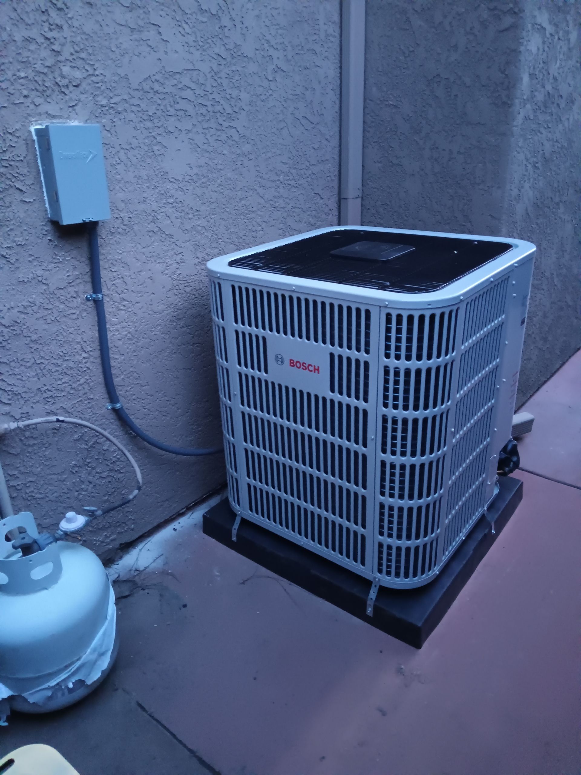 Air conditioning unit, Bosch brand, next to a propane tank and electrical box on a patio.