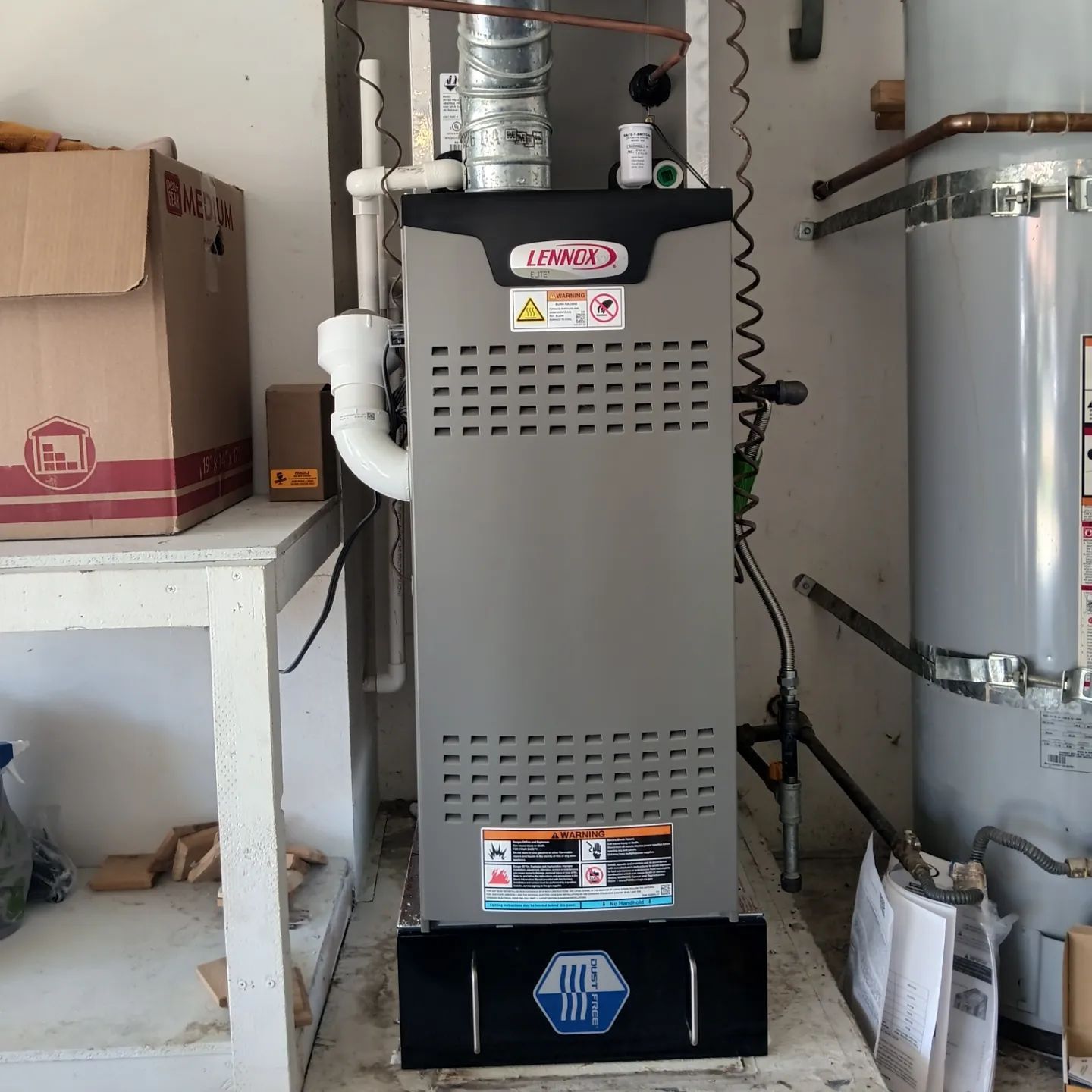 A Lennox furnace in a garage with a hot water heater and a cardboard box.