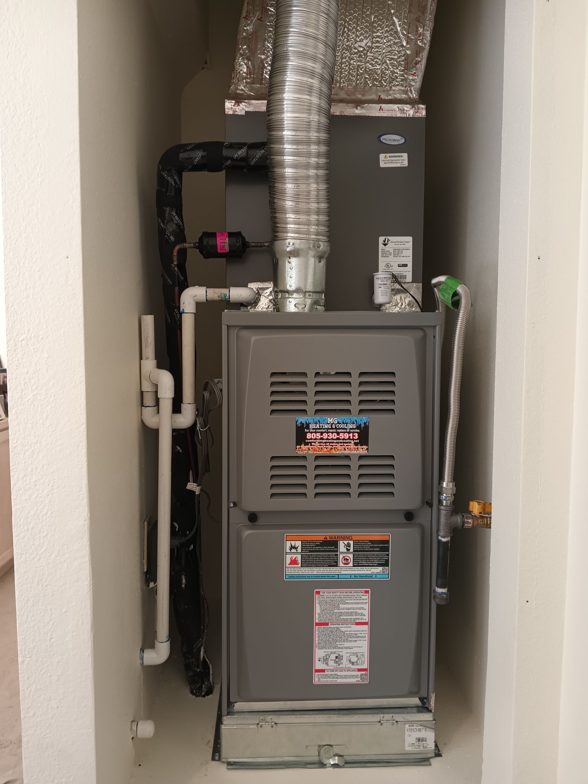 Furnace unit in a white alcove with silver ductwork, pipes and controls.