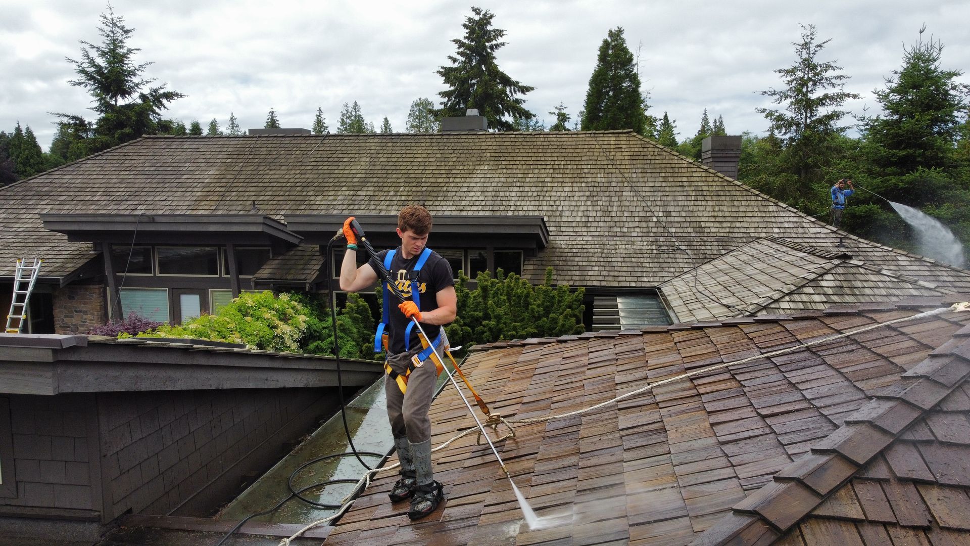 a man is cleaning the roof of a house with a high-pressure washer.