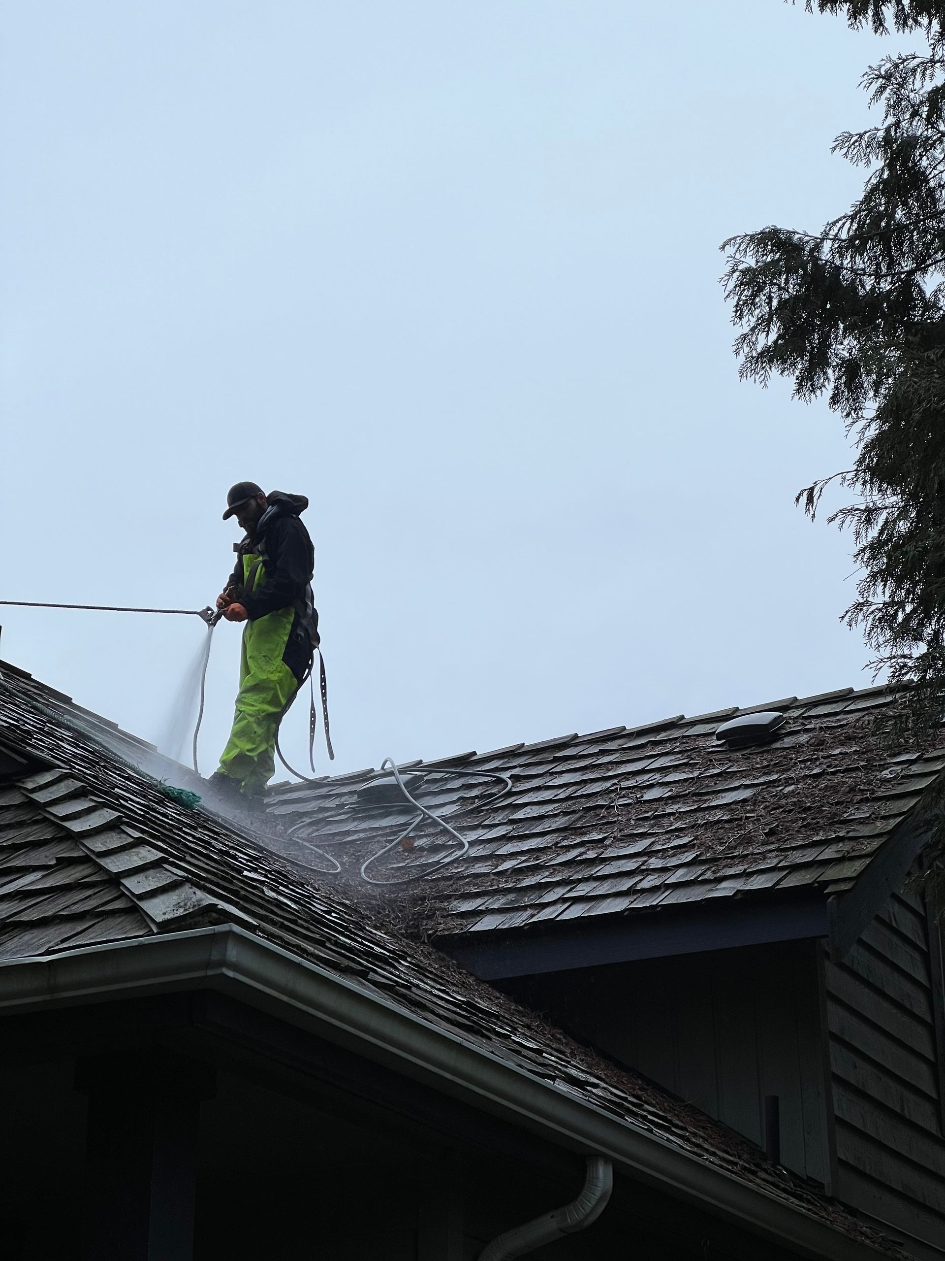 a man is cleaning the roof of a house with a high pressure washer.