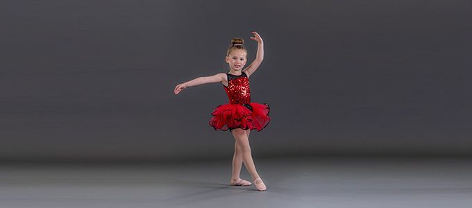 A little girl in a red is dancing on a gray background.