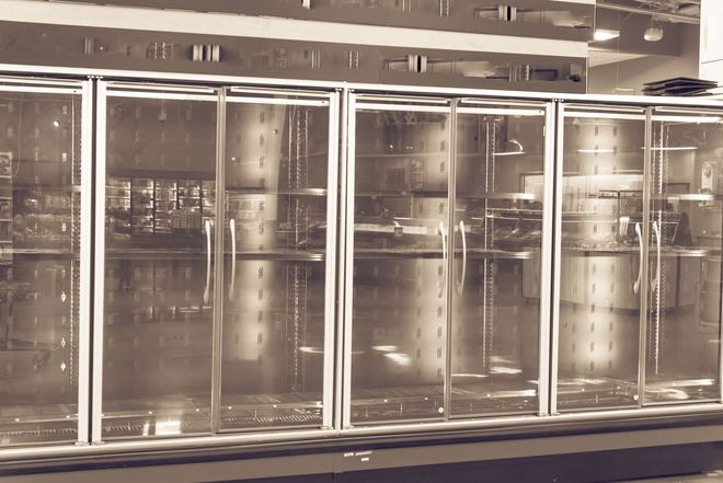 Closed glass-front refrigerated display cases in a supermarket aisle with bright overhead lighting