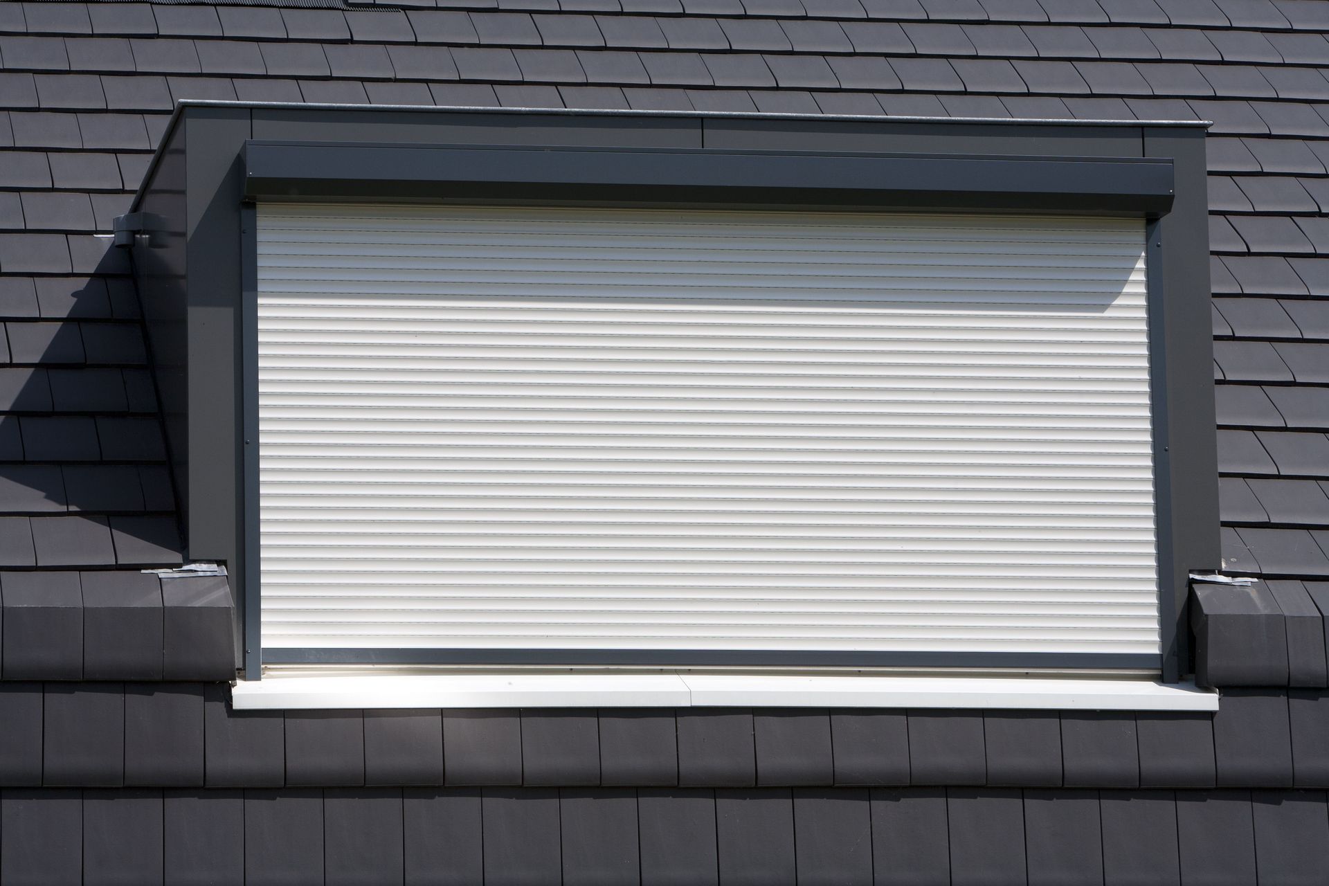 Closed white window shutter on a gray shingled building