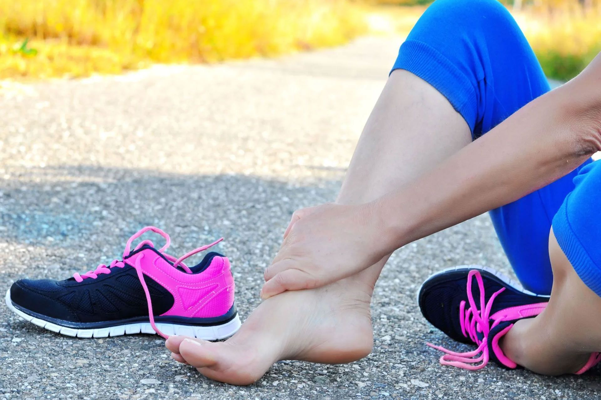 A woman is sitting on the ground with her foot in pain.