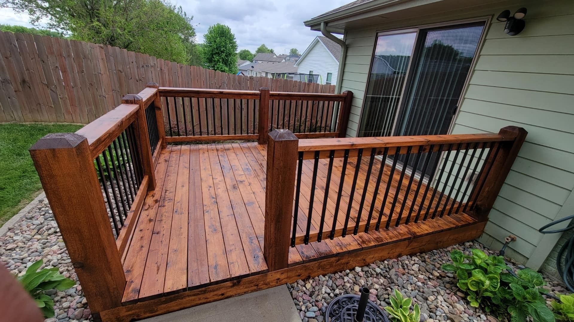 A wooden deck with a railing is in the backyard of a house.