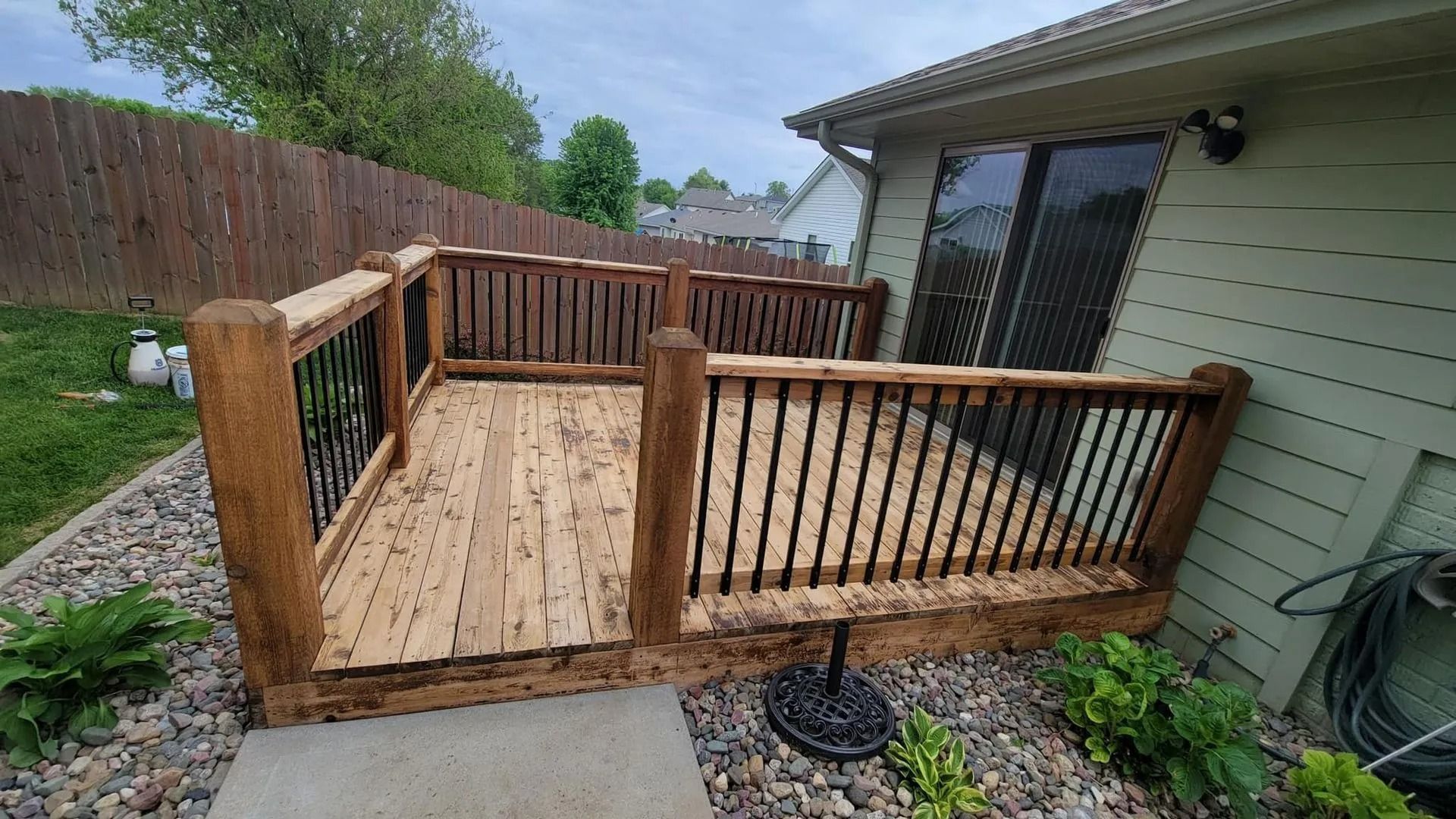 A wooden deck with a metal railing is in the backyard of a house.
