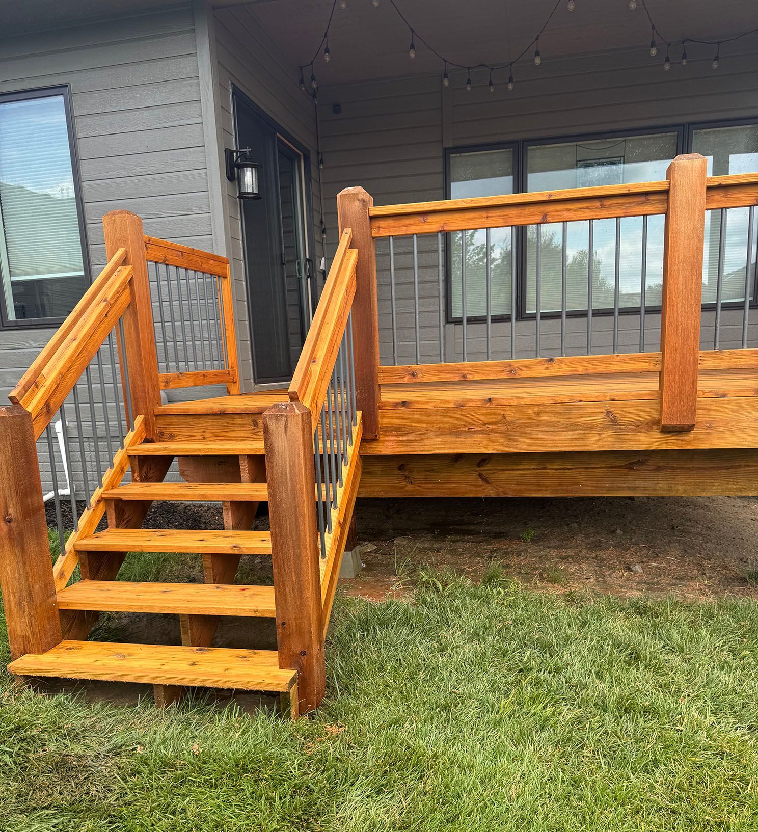 A close up of a wooden deck with a railing and grass in the background.