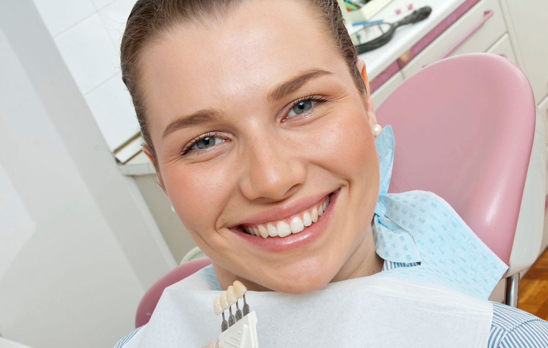 A woman is smiling in a dental chair while holding a model of her teeth.