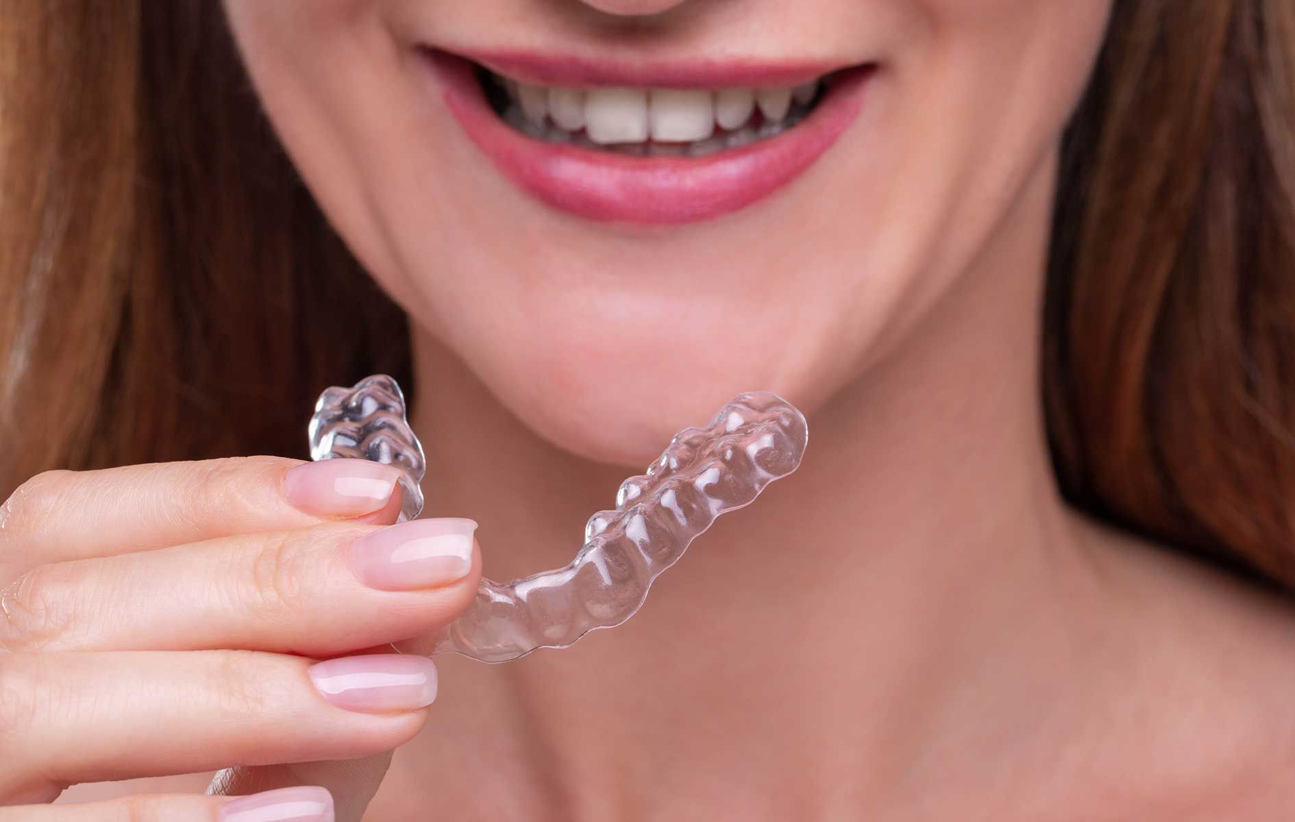 A woman is holding a clear brace in front of her mouth.