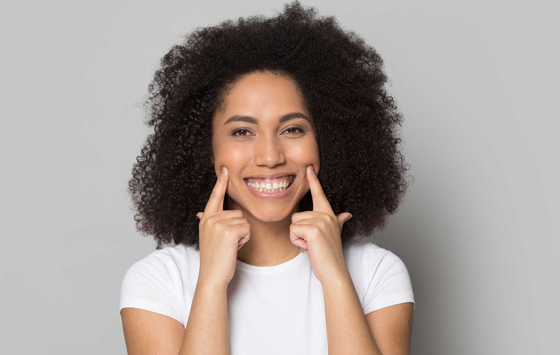 A woman with curly hair is smiling and pointing at her teeth.