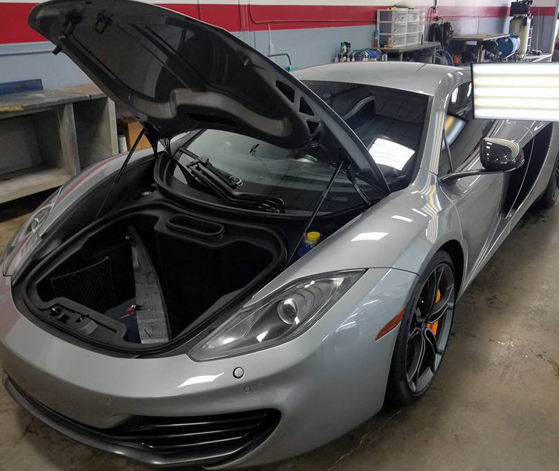 A silver sports car with the hood open in a garage
