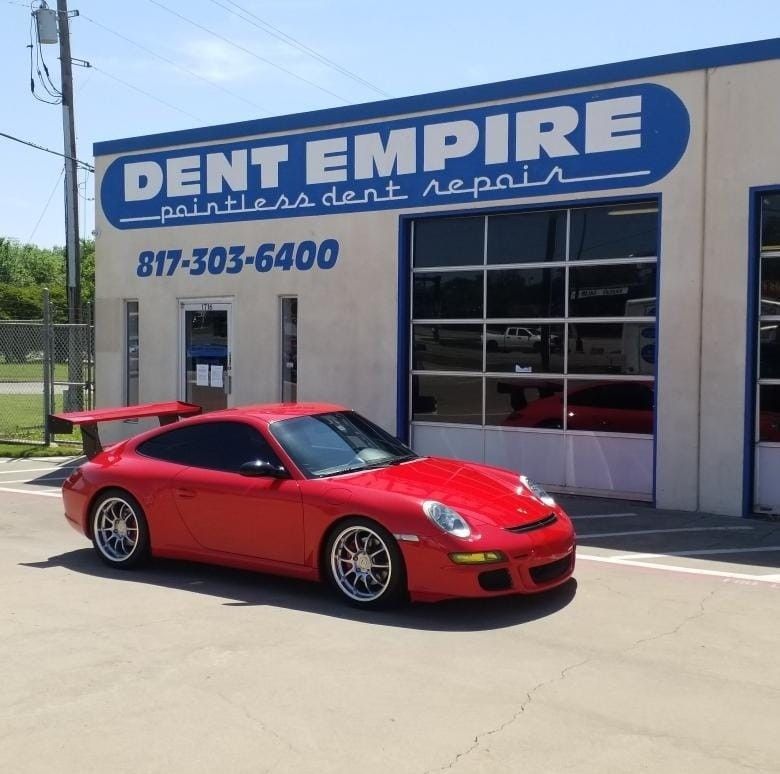 A red car is parked in front of a building that says dent empire paintless dent repair