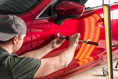 A man is working on a red car with a hammer.