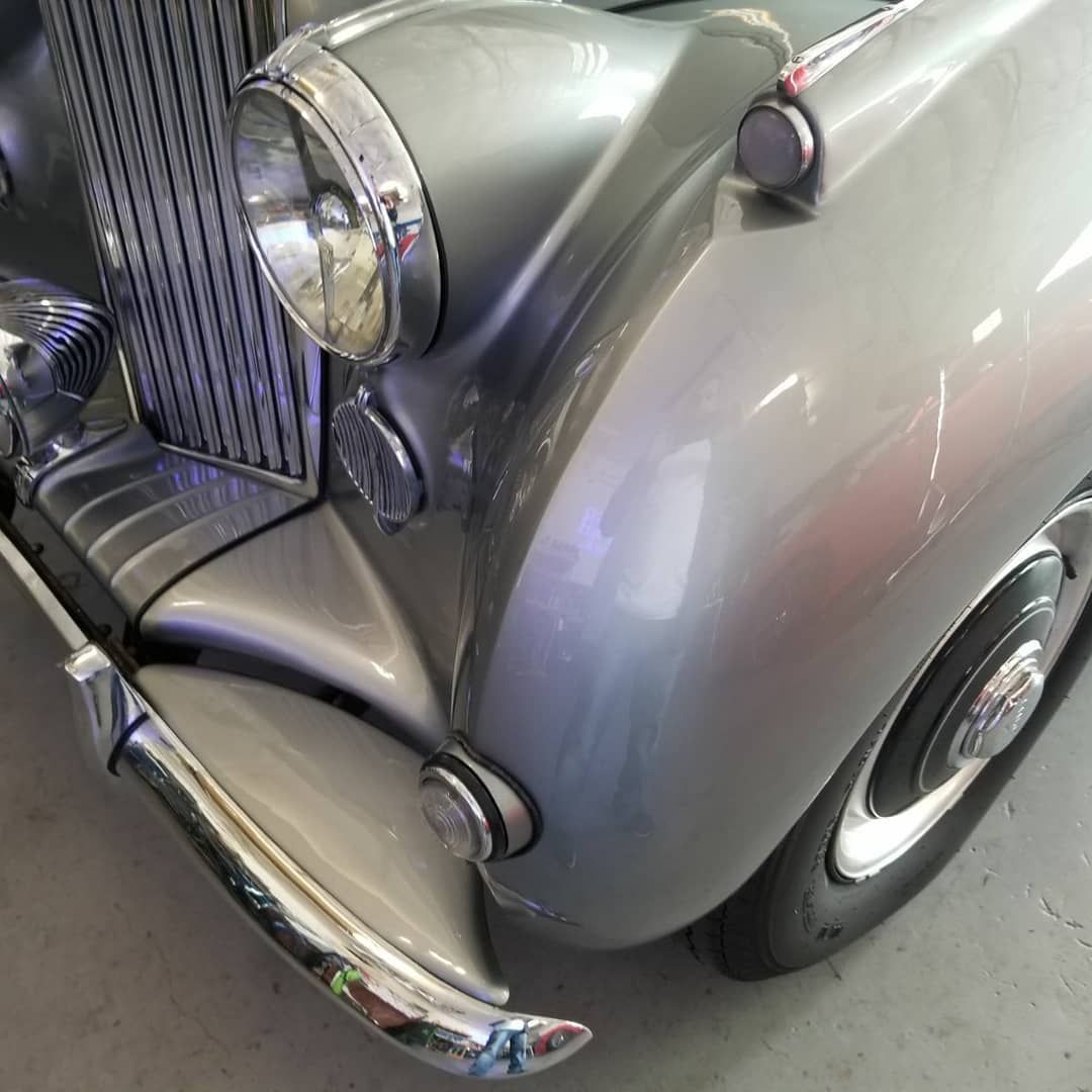 A close up of the front of an old silver car.