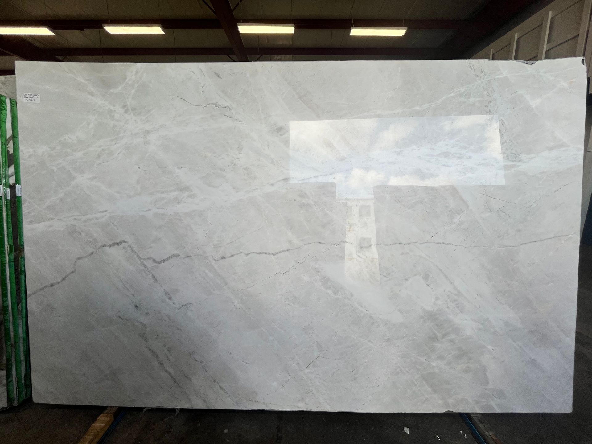 Large white stone slab with subtle gray veining displayed indoors under overhead lights.