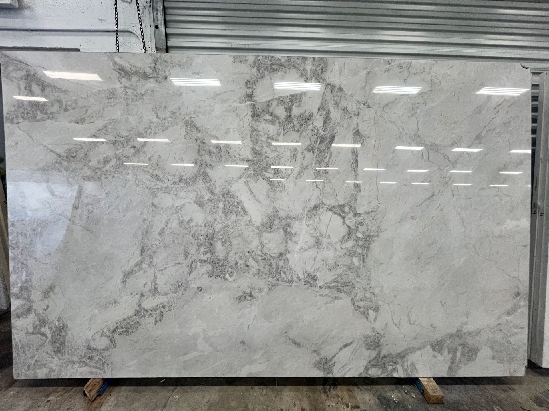 Large white marble slab with gray veining leaning against a metal shutter in a warehouse setting