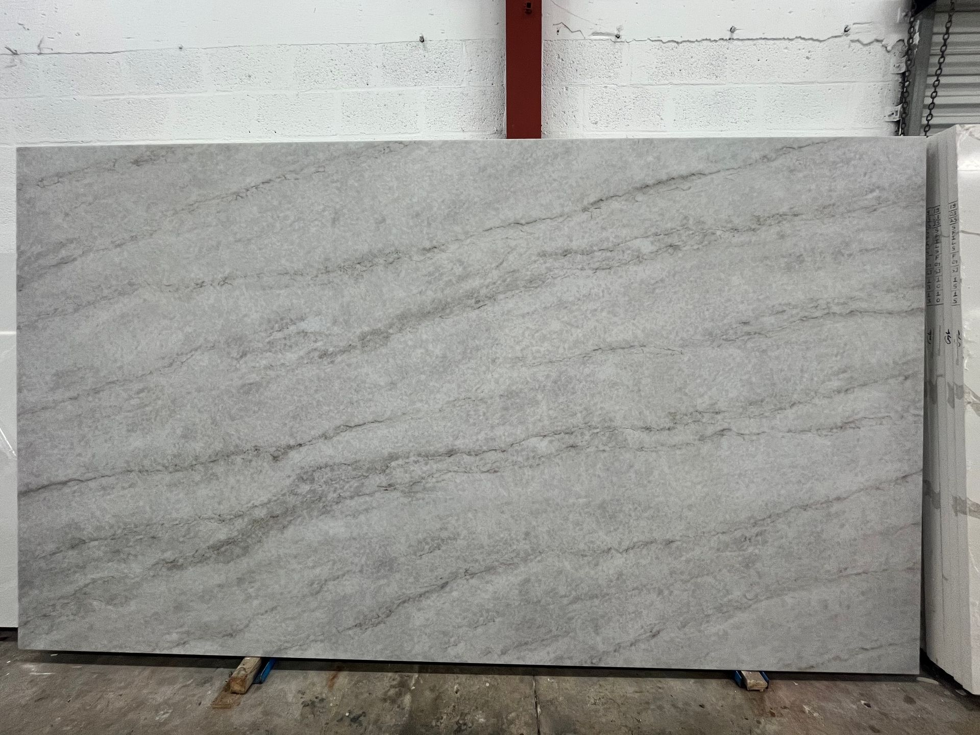 Large light gray marble slab with subtle veining, leaning against a wall in a warehouse or showroom