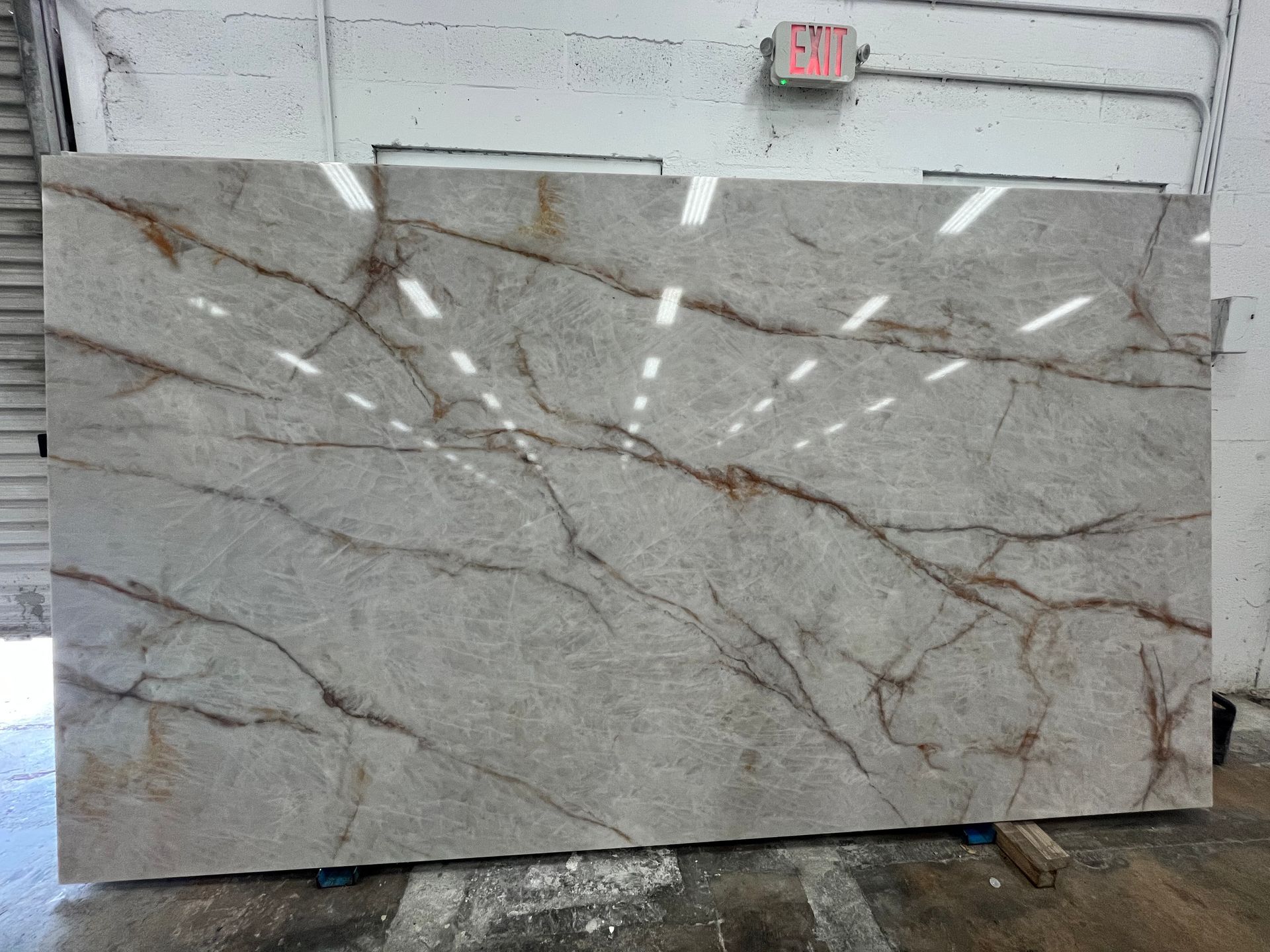 Large gray marble slab with dark veining displayed upright in a warehouse or showroom.