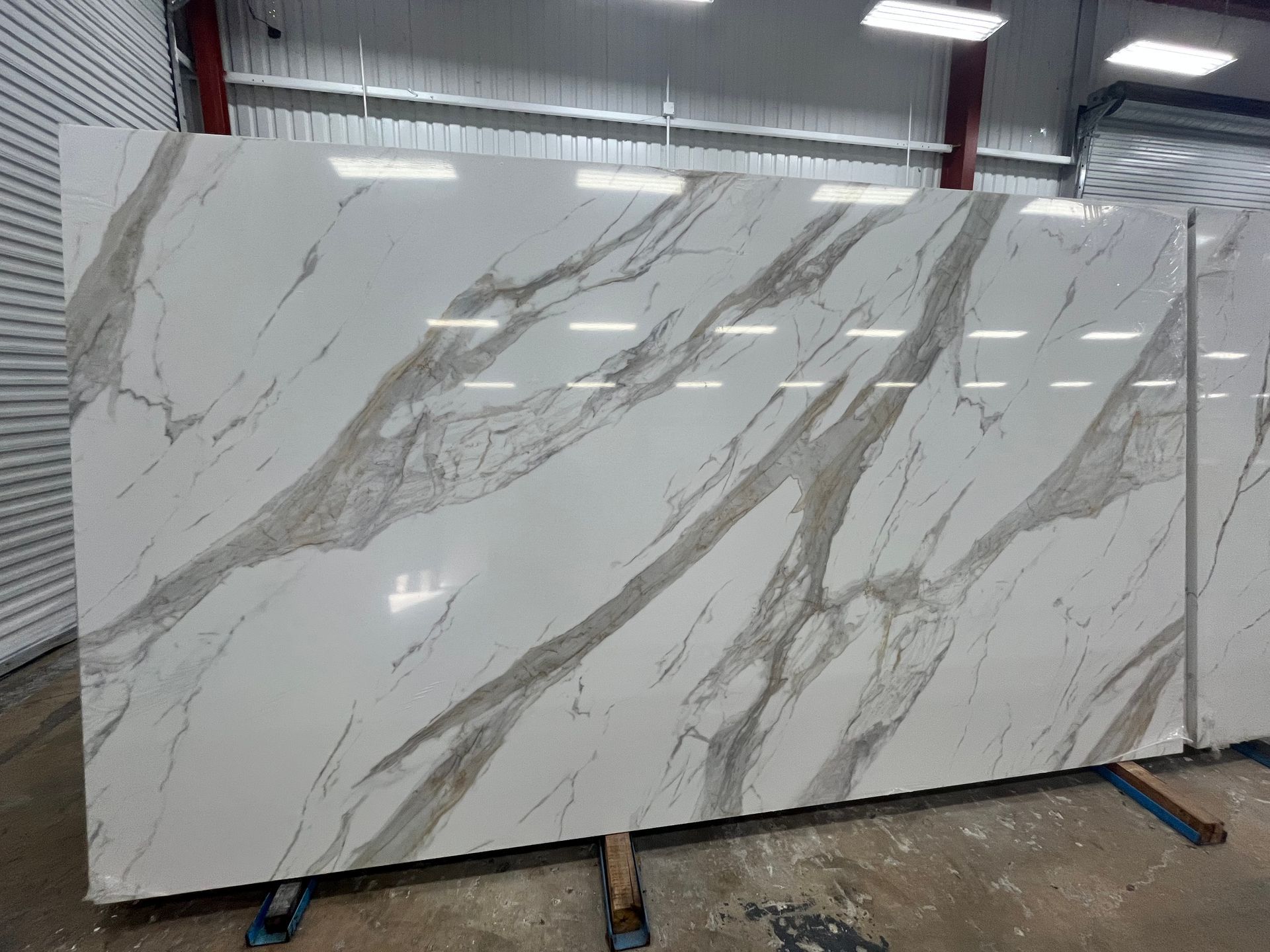 Large white marble slab with gray veining displayed upright in a warehouse.
