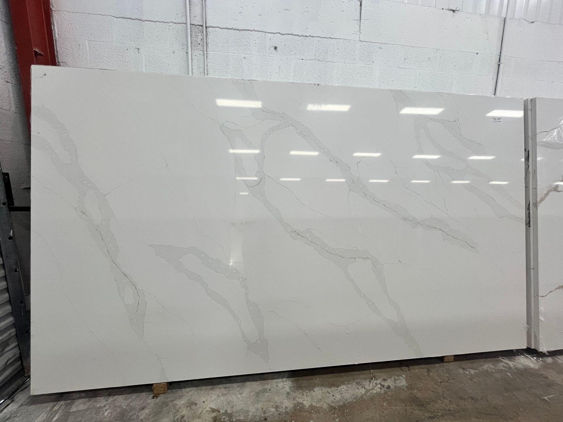 Large white polished stone slab with subtle gray veining, displayed upright in a warehouse.