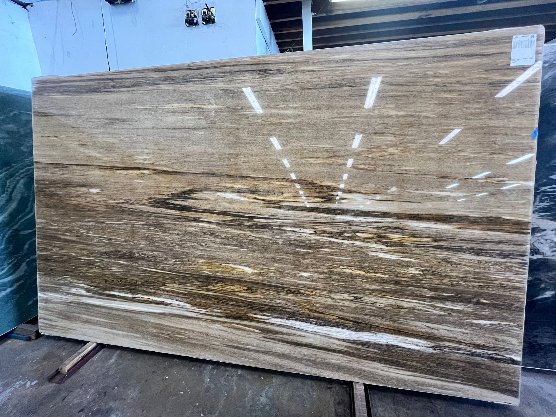 Large tan-and-brown marble slab leaning against a wall in a warehouse