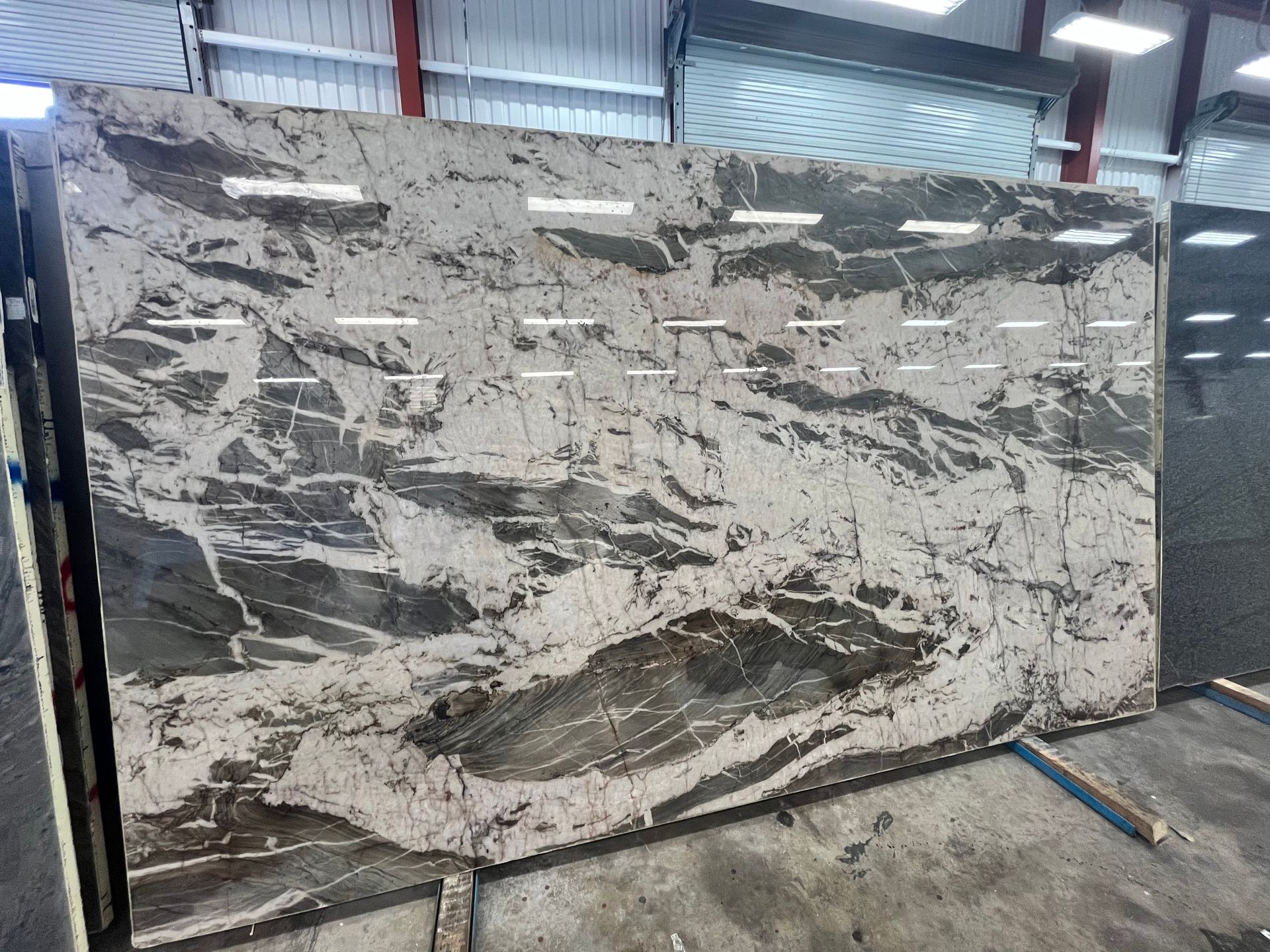 Large abstract mural or painted panel with gray, white, and black brushstrokes in an industrial workshop.