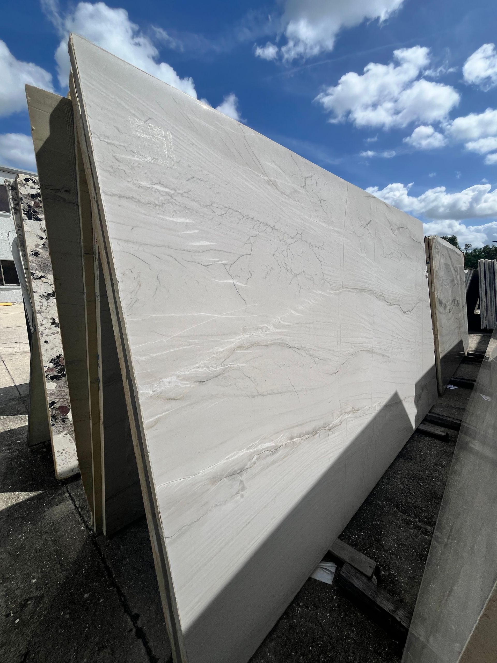 Stacked large white stone slabs outdoors in a storage yard under a blue sky.