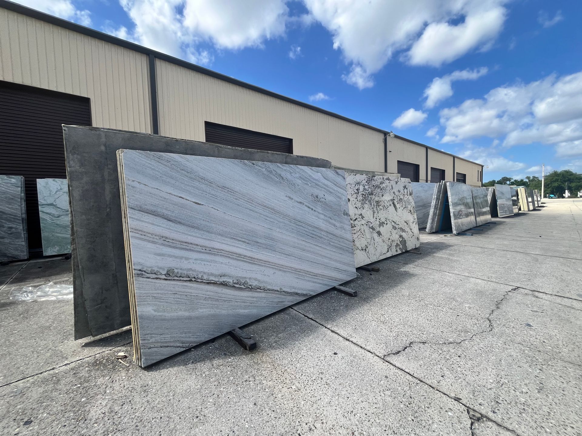 Several large, rectangular stone slabs with varied patterns and colors stand upright in a row outdoors on a paved lot.